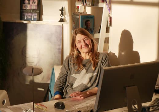 A woman sitting at a desk in a sunlit room smiling.