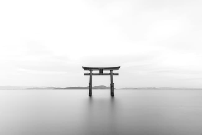 Japanese gate on a lake-like surface in black and white - very serene landscape.